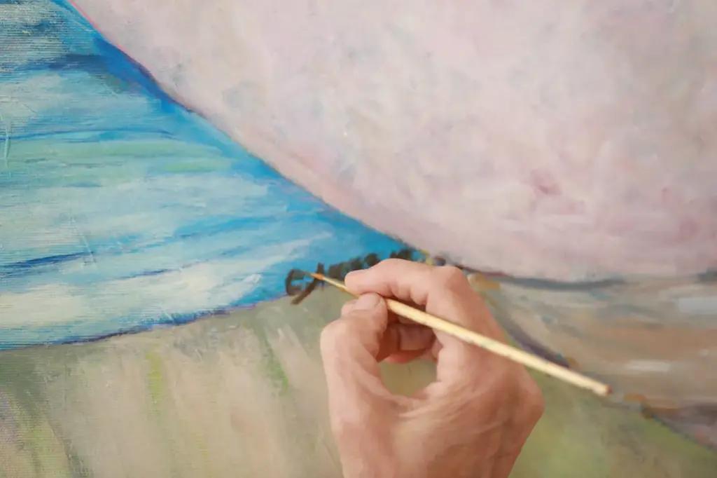 The hand of the artist signing a canvas with a fine brush